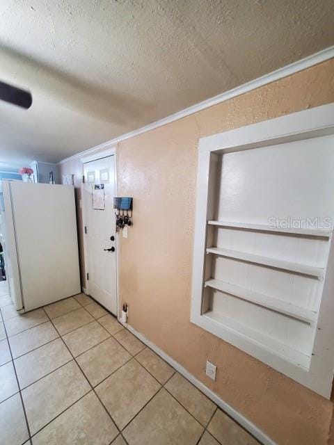 doorway to outside with crown molding, light tile patterned floors, a textured ceiling, and built in shelves