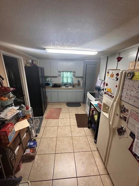 kitchen with white fridge with ice dispenser, black refrigerator, a textured ceiling, and light tile patterned floors