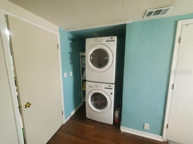 laundry room featuring dark hardwood / wood-style flooring, a textured ceiling, and stacked washing maching and dryer