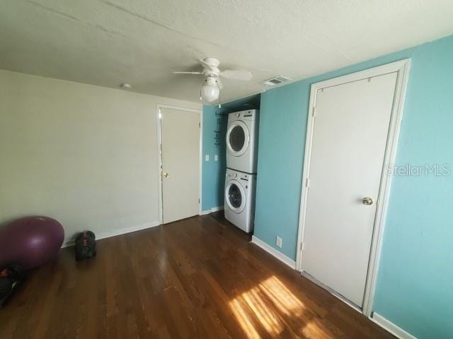 washroom with dark wood-type flooring, stacked washer and dryer, and ceiling fan