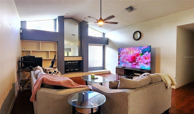 living room with ceiling fan, a tile fireplace, high vaulted ceiling, built in features, and hardwood / wood-style floors