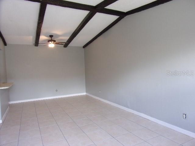 empty room featuring lofted ceiling with beams, ceiling fan, and light tile patterned floors