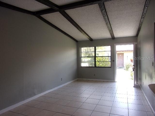 unfurnished room with lofted ceiling with beams, light tile patterned floors, and a textured ceiling