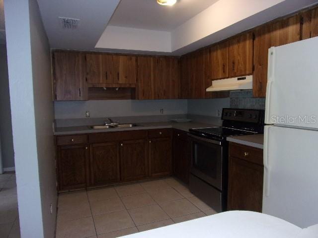 kitchen with black electric range oven, backsplash, white refrigerator, sink, and light tile patterned flooring