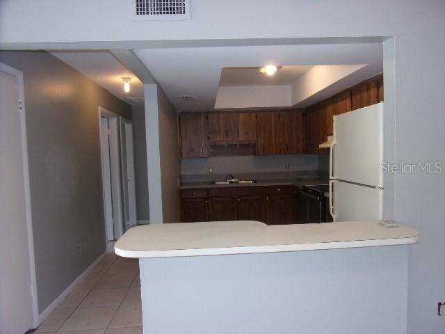 kitchen featuring white fridge, kitchen peninsula, sink, and light tile patterned floors