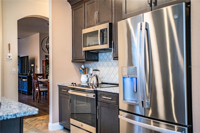 kitchen featuring backsplash, dark brown cabinetry, light stone counters, and appliances with stainless steel finishes