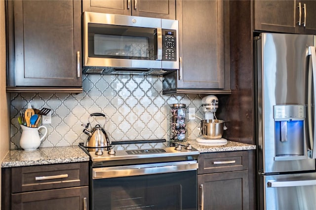 kitchen featuring light stone counters, dark brown cabinetry, appliances with stainless steel finishes, and tasteful backsplash