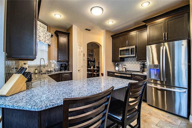 kitchen with backsplash, sink, a breakfast bar area, light stone counters, and stainless steel appliances