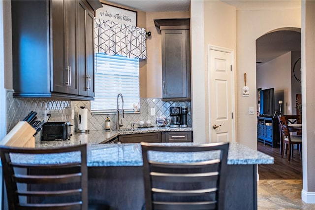 kitchen featuring kitchen peninsula, light stone counters, a breakfast bar area, and sink