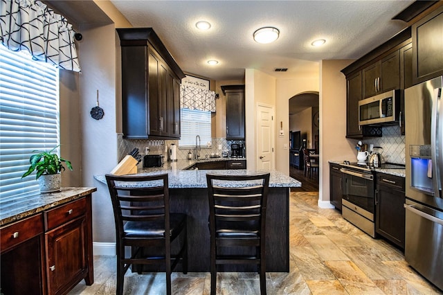 kitchen featuring pendant lighting, a breakfast bar, tasteful backsplash, light stone counters, and stainless steel appliances