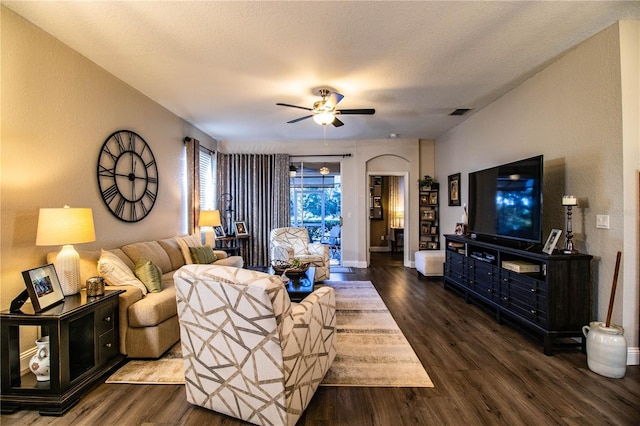 living room with a textured ceiling, ceiling fan, and dark wood-type flooring