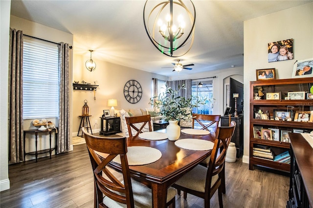 dining space with dark hardwood / wood-style flooring, ceiling fan with notable chandelier, and a healthy amount of sunlight