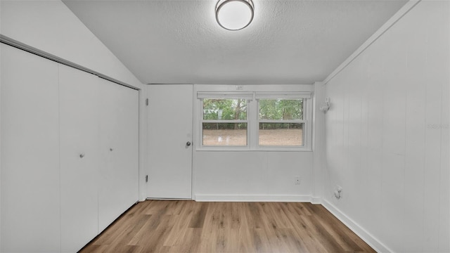 spare room with vaulted ceiling, a textured ceiling, and light wood-type flooring