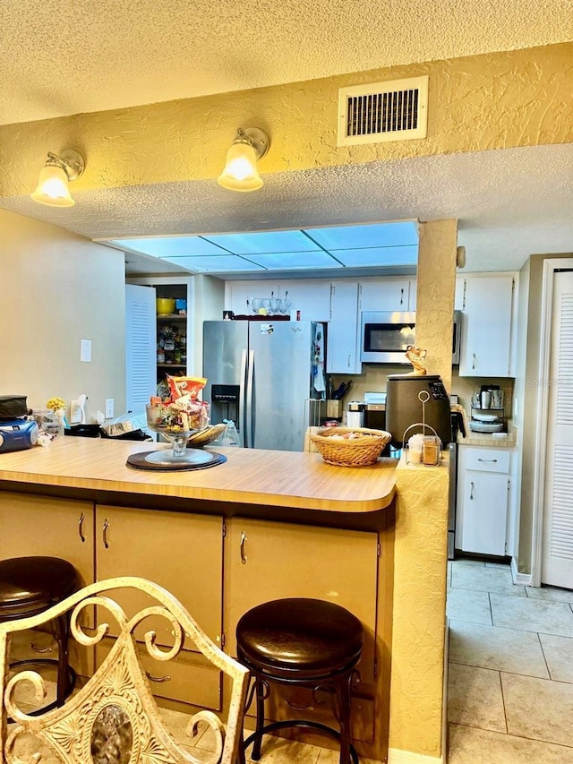 kitchen featuring stainless steel appliances, butcher block countertops, kitchen peninsula, a breakfast bar, and light tile patterned floors