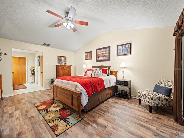 bedroom featuring a textured ceiling, ceiling fan, light hardwood / wood-style floors, and lofted ceiling