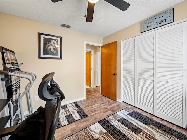 workout room with hardwood / wood-style flooring, ceiling fan, and a textured ceiling