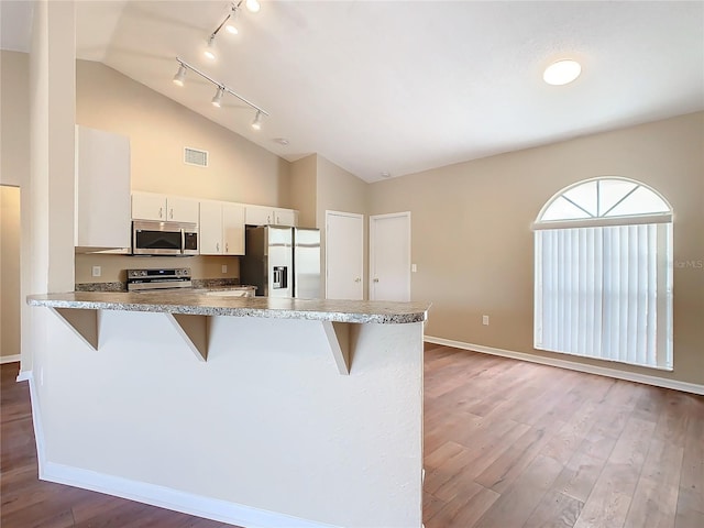 kitchen with white cabinets, wood-type flooring, stainless steel appliances, kitchen peninsula, and a breakfast bar area