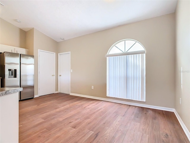 kitchen featuring white cabinets, vaulted ceiling, light hardwood / wood-style flooring, and stainless steel fridge