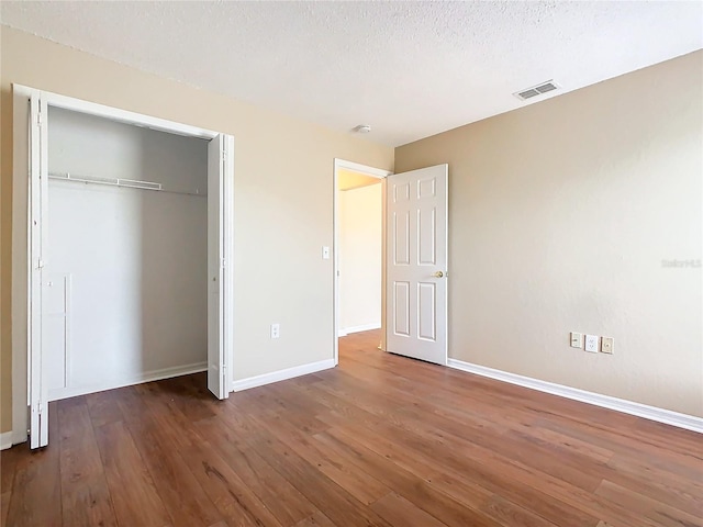 unfurnished bedroom with a textured ceiling, dark hardwood / wood-style floors, and a closet