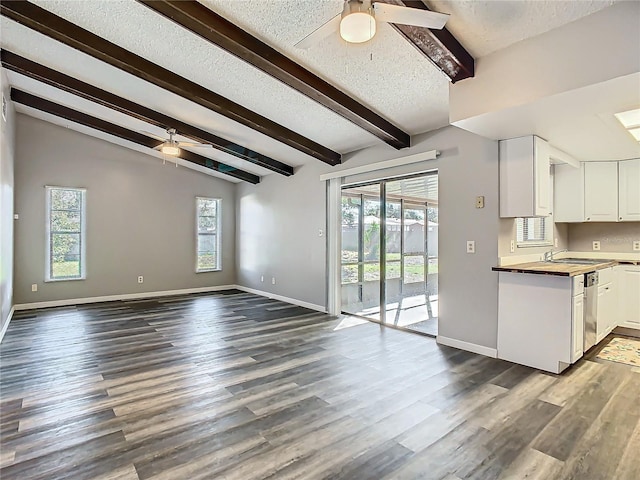 unfurnished living room with vaulted ceiling with beams, ceiling fan, dark hardwood / wood-style floors, and a textured ceiling