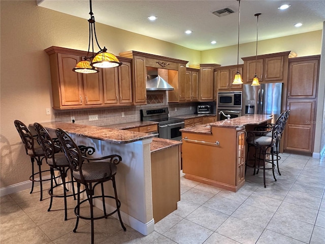 kitchen with a center island with sink, hanging light fixtures, a breakfast bar area, wall chimney exhaust hood, and stainless steel appliances