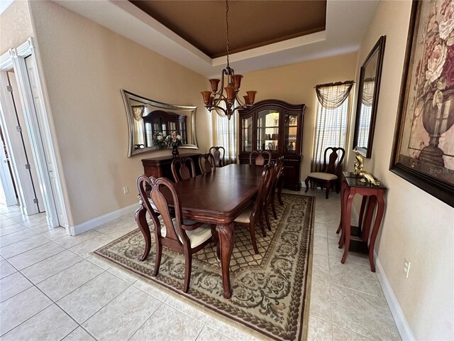 tiled dining space featuring an inviting chandelier and a raised ceiling