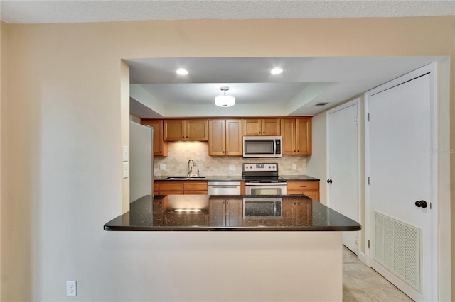 kitchen featuring dark stone counters, kitchen peninsula, sink, and stainless steel appliances