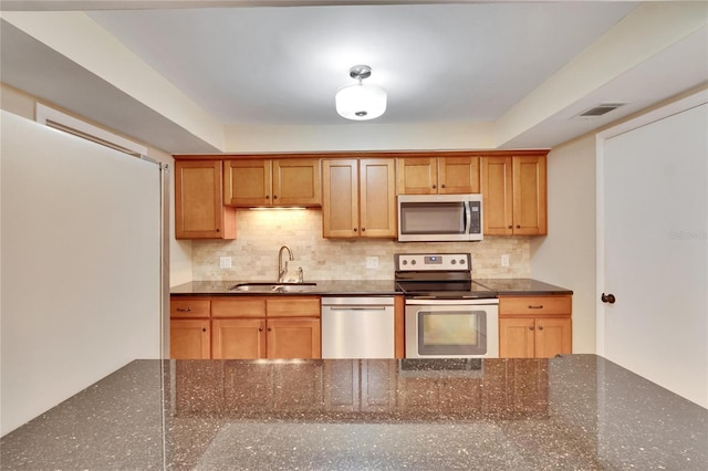 kitchen with backsplash, sink, dark stone counters, and appliances with stainless steel finishes