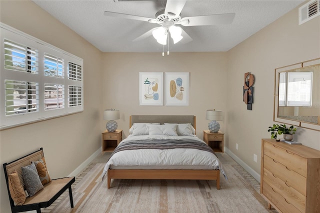 bedroom featuring a textured ceiling, ceiling fan, visible vents, and baseboards