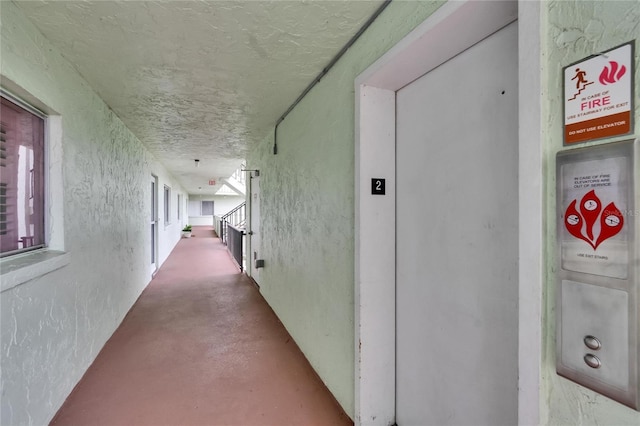 hall with finished concrete floors, a textured wall, and stairway