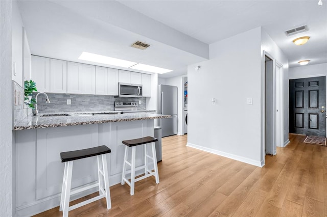 kitchen with kitchen peninsula, light stone countertops, stainless steel appliances, sink, and white cabinetry