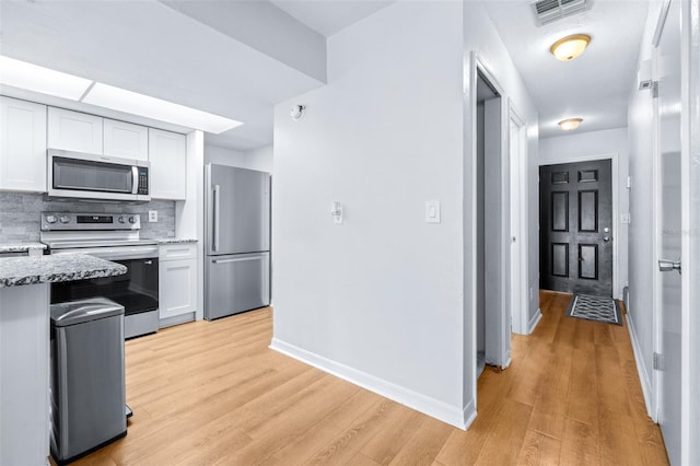 kitchen with white cabinetry, light stone countertops, light hardwood / wood-style flooring, decorative backsplash, and appliances with stainless steel finishes