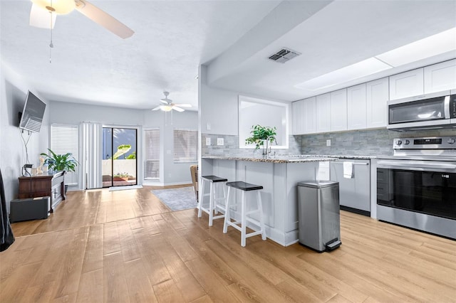 kitchen featuring white cabinetry, stainless steel appliances, a kitchen breakfast bar, kitchen peninsula, and decorative backsplash