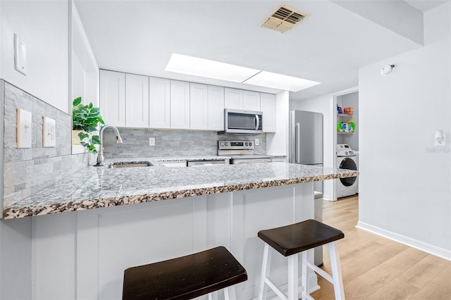 kitchen with sink, tasteful backsplash, kitchen peninsula, washer / dryer, and appliances with stainless steel finishes