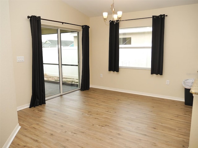 unfurnished room with an inviting chandelier, light wood finished floors, baseboards, and vaulted ceiling