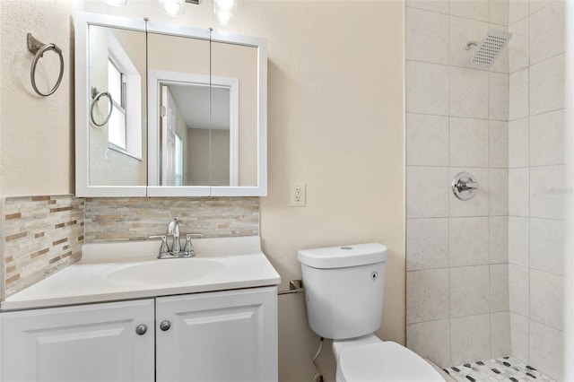 bathroom featuring vanity, backsplash, tiled shower, and toilet