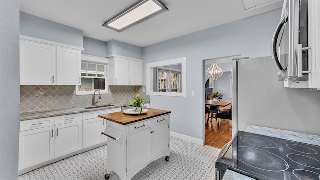 kitchen featuring wood counters, backsplash, white cabinets, sink, and range