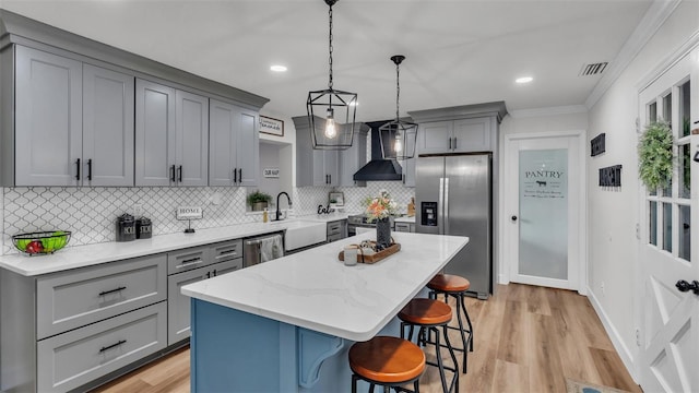 kitchen featuring a kitchen bar, wall chimney exhaust hood, stainless steel appliances, decorative light fixtures, and a center island