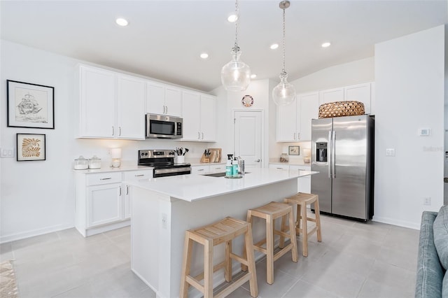 kitchen featuring white cabinets, stainless steel appliances, an island with sink, hanging light fixtures, and a breakfast bar