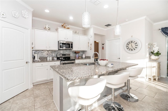 kitchen featuring stainless steel appliances, sink, white cabinetry, hanging light fixtures, and an island with sink