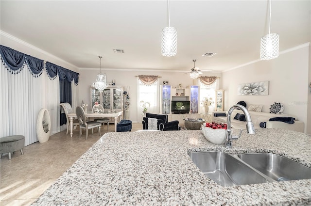 kitchen with light stone counters, ornamental molding, ceiling fan, sink, and hanging light fixtures