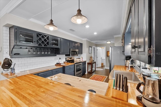 kitchen with decorative backsplash, stainless steel appliances, butcher block countertops, and hanging light fixtures