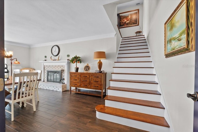 stairs with hardwood / wood-style floors, crown molding, and a brick fireplace