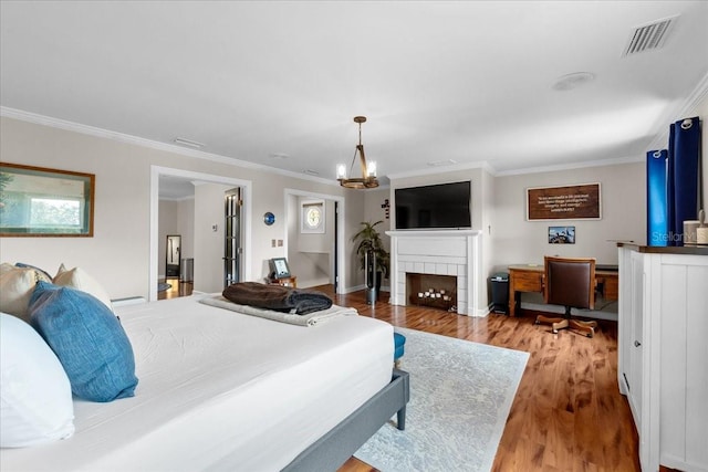 bedroom with a fireplace, ornamental molding, a notable chandelier, and light wood-type flooring