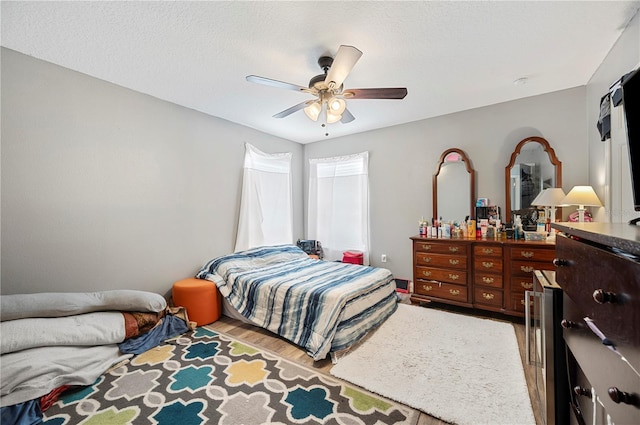 bedroom with ceiling fan, light hardwood / wood-style flooring, beverage cooler, and a textured ceiling