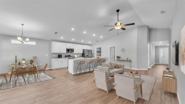 living area featuring visible vents, baseboards, light wood-type flooring, ceiling fan with notable chandelier, and high vaulted ceiling