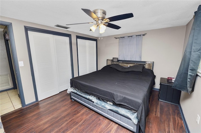 bedroom featuring ceiling fan, dark wood-type flooring, a textured ceiling, and multiple closets