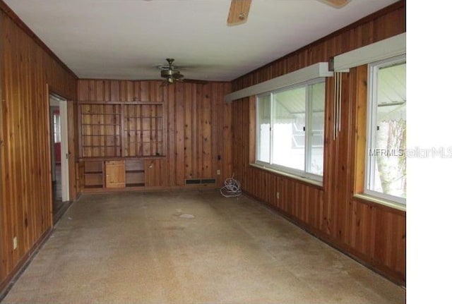 carpeted spare room with wood walls and ceiling fan