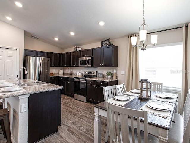 kitchen with stainless steel appliances, hardwood / wood-style floors, pendant lighting, lofted ceiling, and a kitchen island with sink