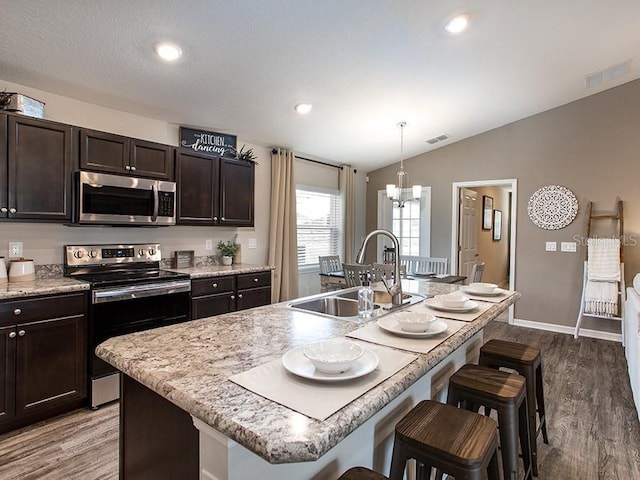 kitchen with hardwood / wood-style floors, sink, stainless steel appliances, and a kitchen island with sink